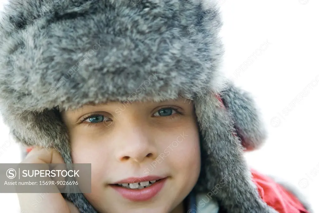 Boy wearing fur hat, smiling at camera, close-up