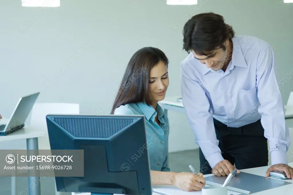 Businesswoman and businessman in office, smiling, writing