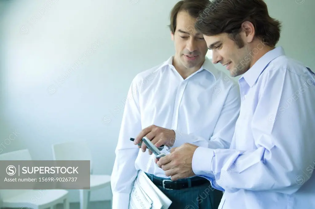 Two businessmen looking at cell phone, pointing, waist up
