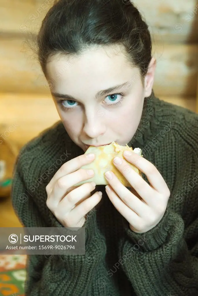 Teenage girl eating crepe, looking at camera