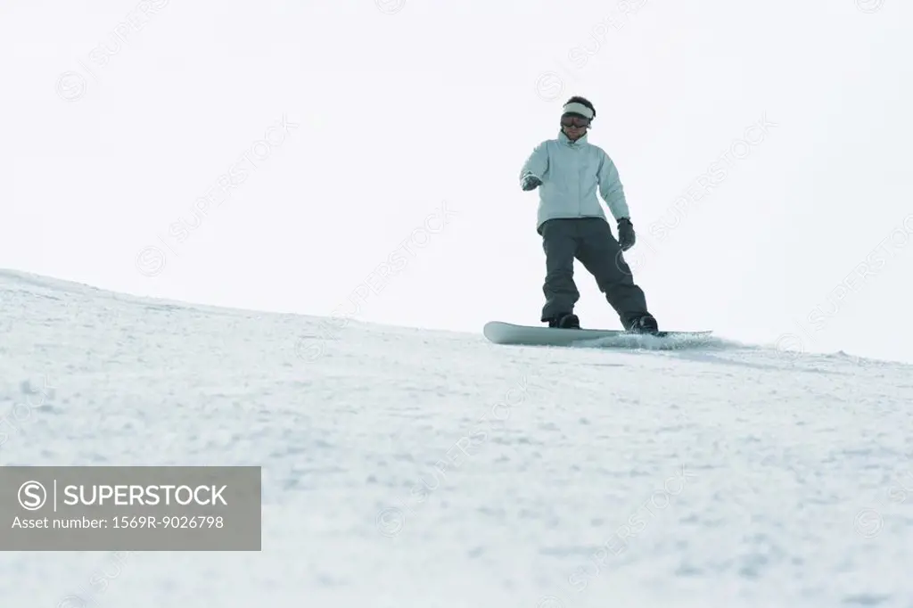 Young man snowboarding on top of ski slope, full length