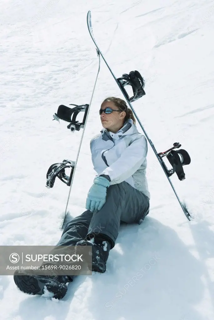Young female skier sitting on the ground under skis, looking away
