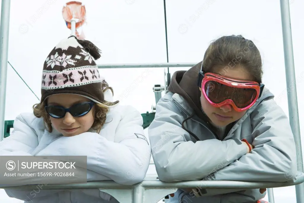 Two teenage girls on chair lift, heads resting on arms, portrait