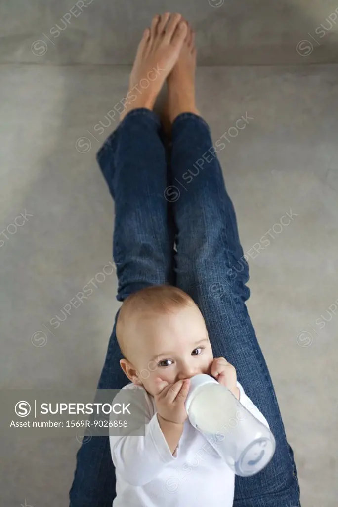 Baby sitting on woman´s lap, drinking from baby bottle