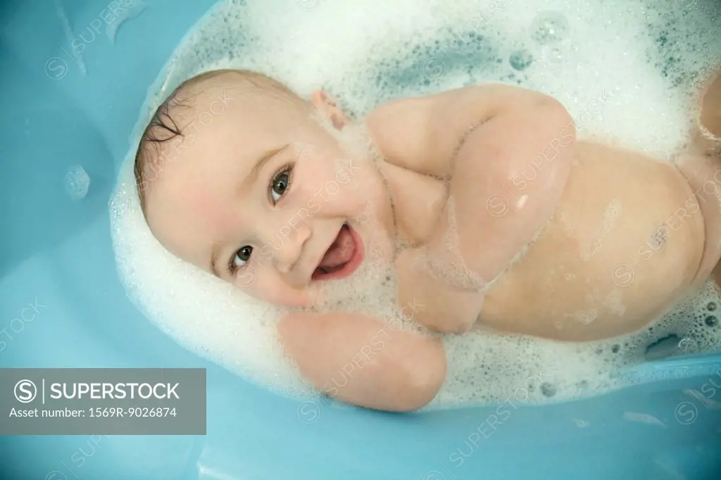 Naked baby in bathtub, smiling at camera