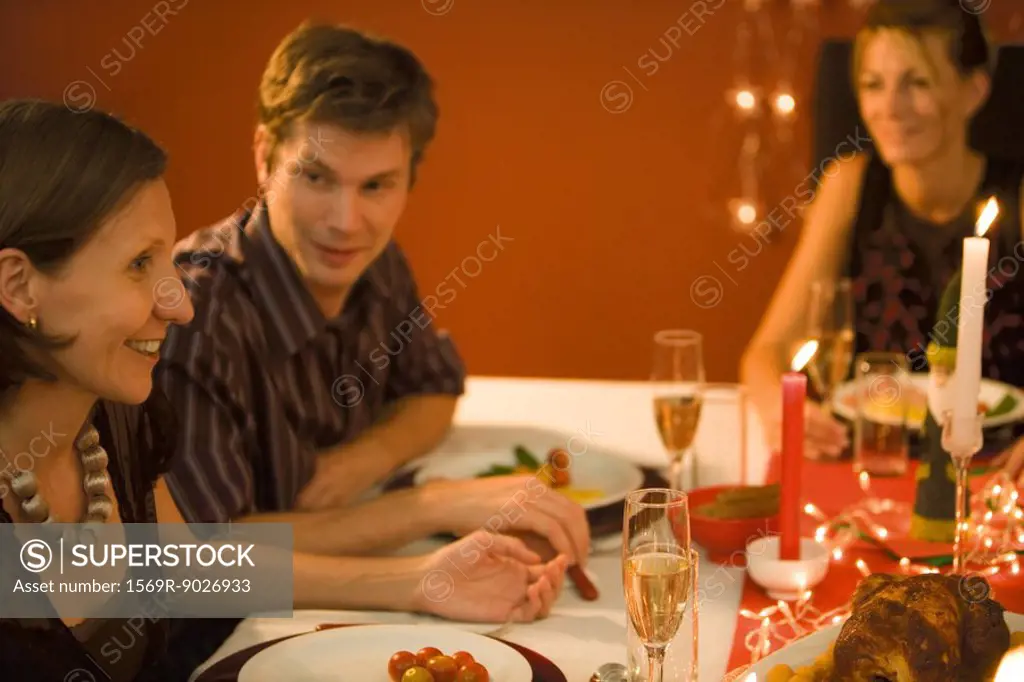 Three adult friends eating Christmas dinner, looking at each other, smiling