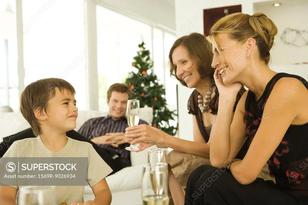 Three adults drinking champagne, smiling at boy, Christmas tree in background