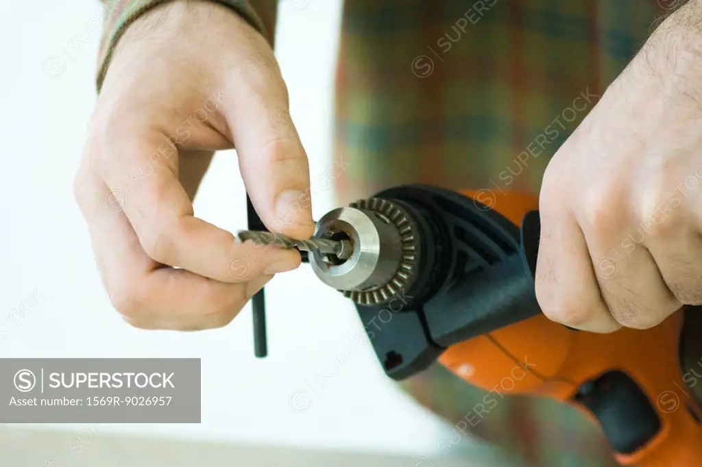 Man adjusting drill bit, cropped view of hands