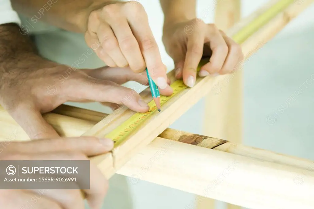 Couple measuring wood with measuring tape, cropped view of hands