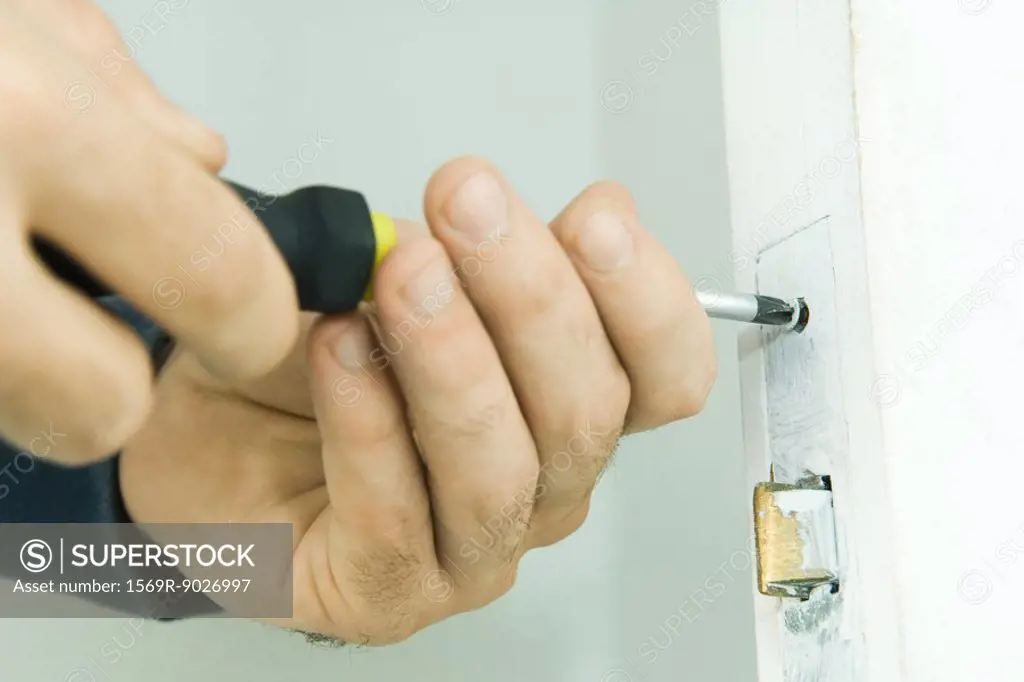 Man repairing door lock with screwdriver, cropped view of hands
