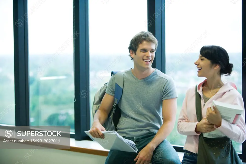 Two students chatting in front of window, smiling at each other