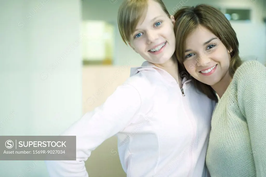 Two young friends standing together, smiling, one leaning her head on the other´s shoulder