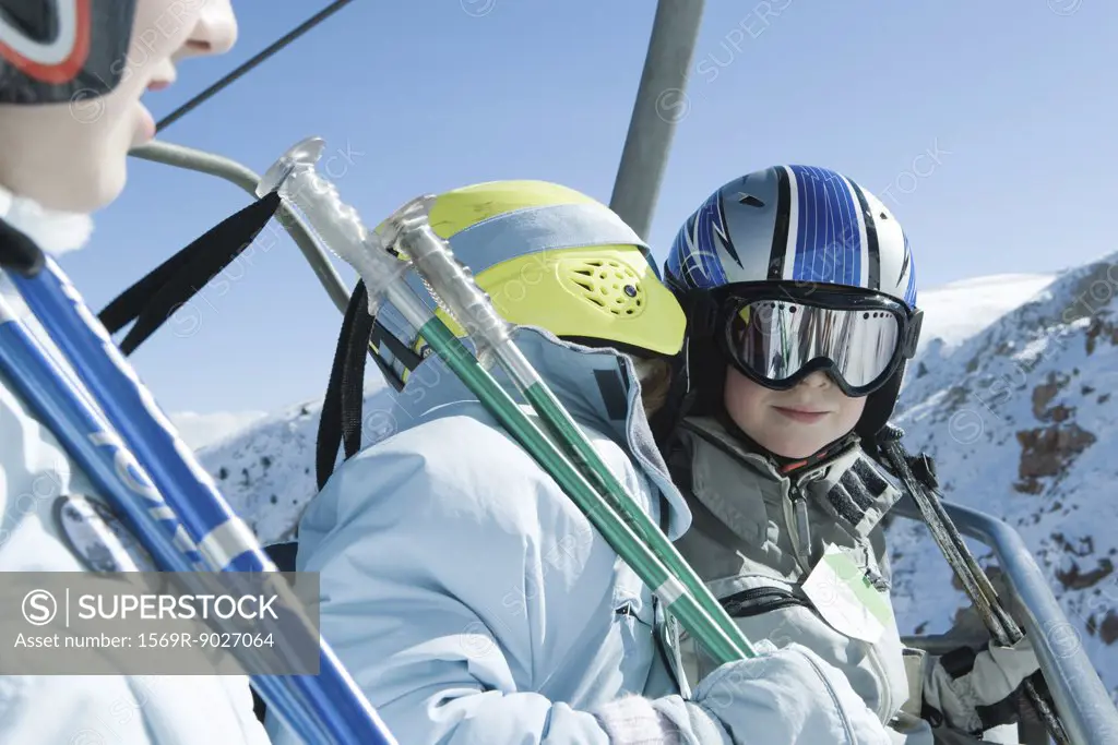 Young skiers on chair lift, one whispering in the other's ear