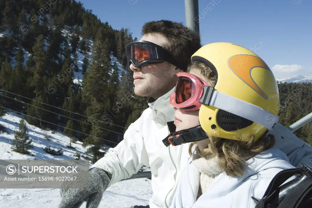 Two young skiers on chair lift, looking away, side view