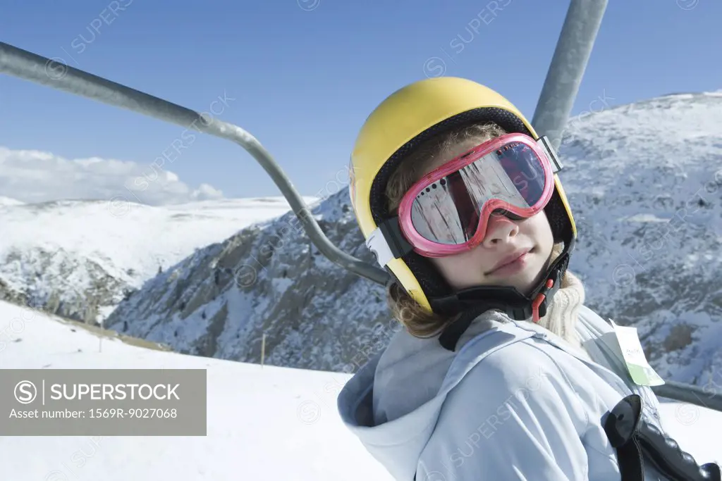 Teenage girl on ski lift, wearing goggles and helmet, looking at camera, portrait