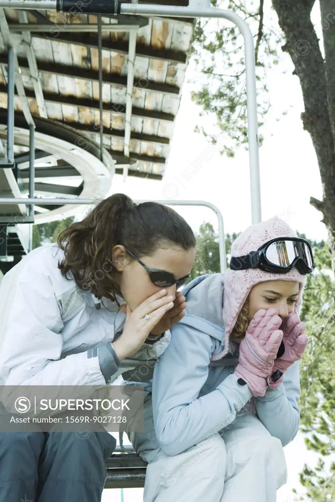 Teenage girls sitting on chair lift together, leaning over, shouting