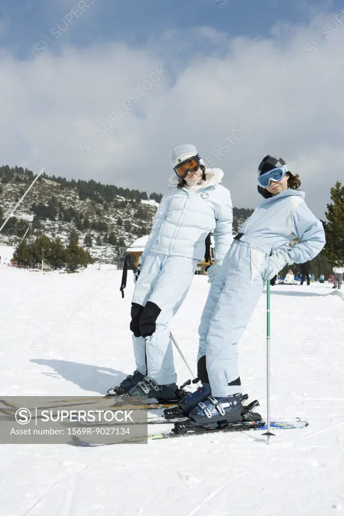 Two young skiers standing, leaning back, smiling at camera