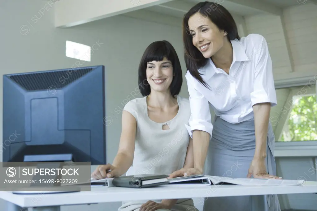 Two businesswomen looking at computer monitor together, smiling