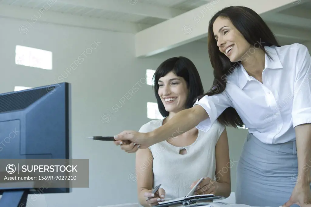Two businesswomen looking at computer monitor together, one pointing