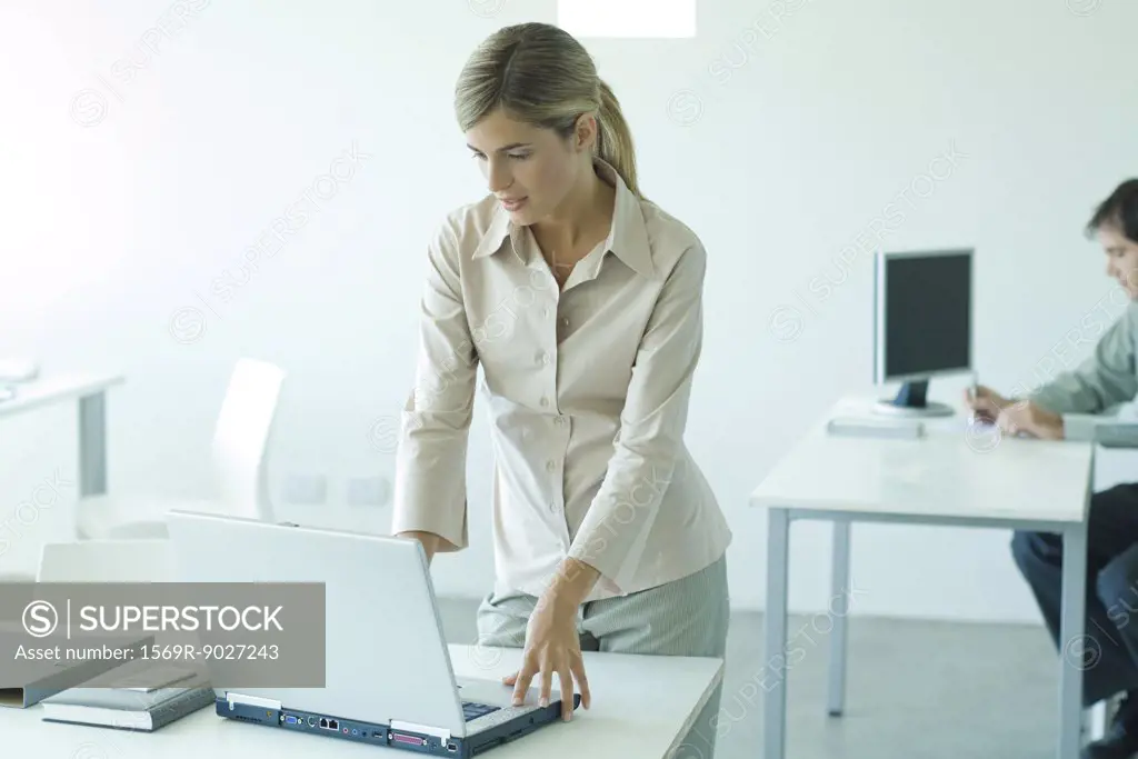 Young businesswoman standing at desk, using laptop
