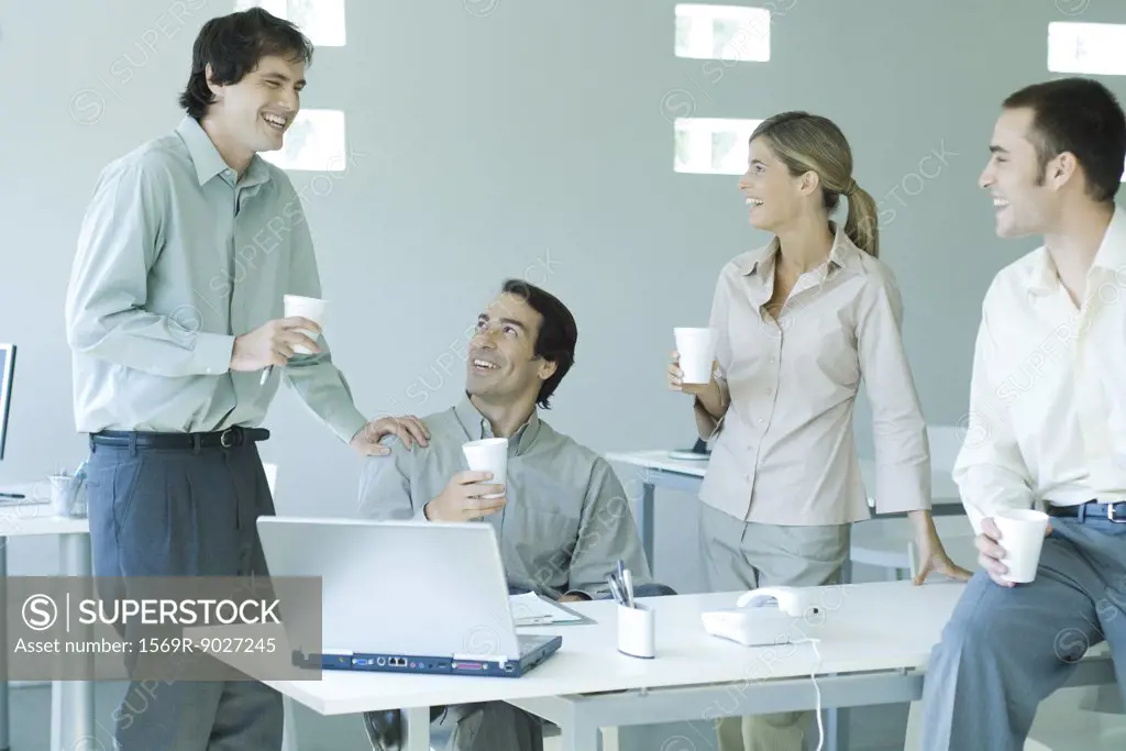 Business associates gathered around table, holding disposable cups, laughing