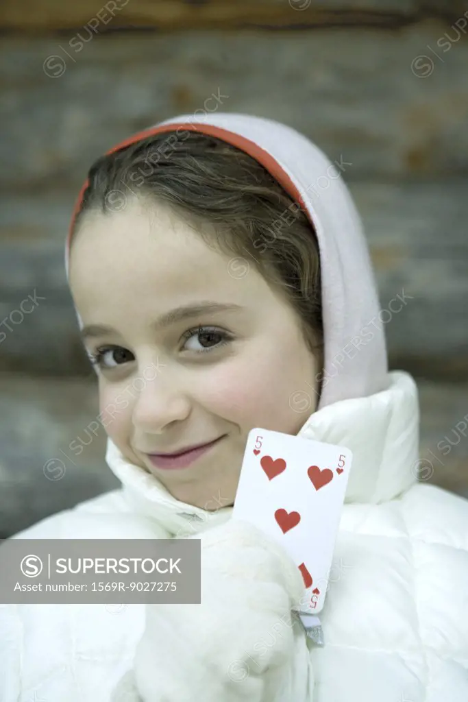 Girl in winter clothes holding up playing card