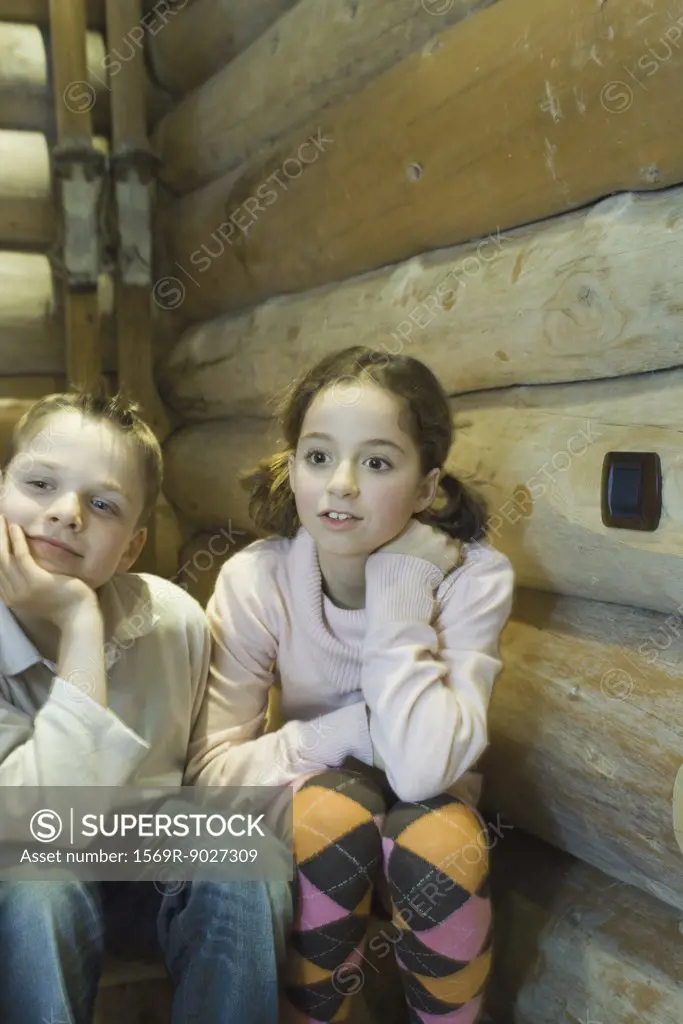 Preteen boy and girl sitting side by side, looking out of frame