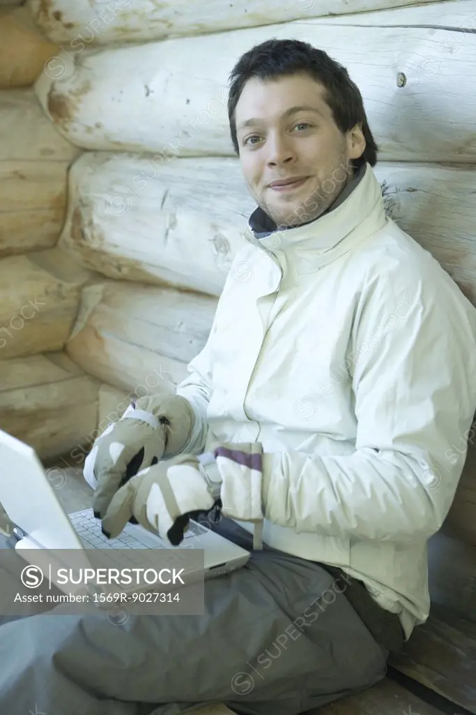 Man using laptop with gloves on, smiling at camera