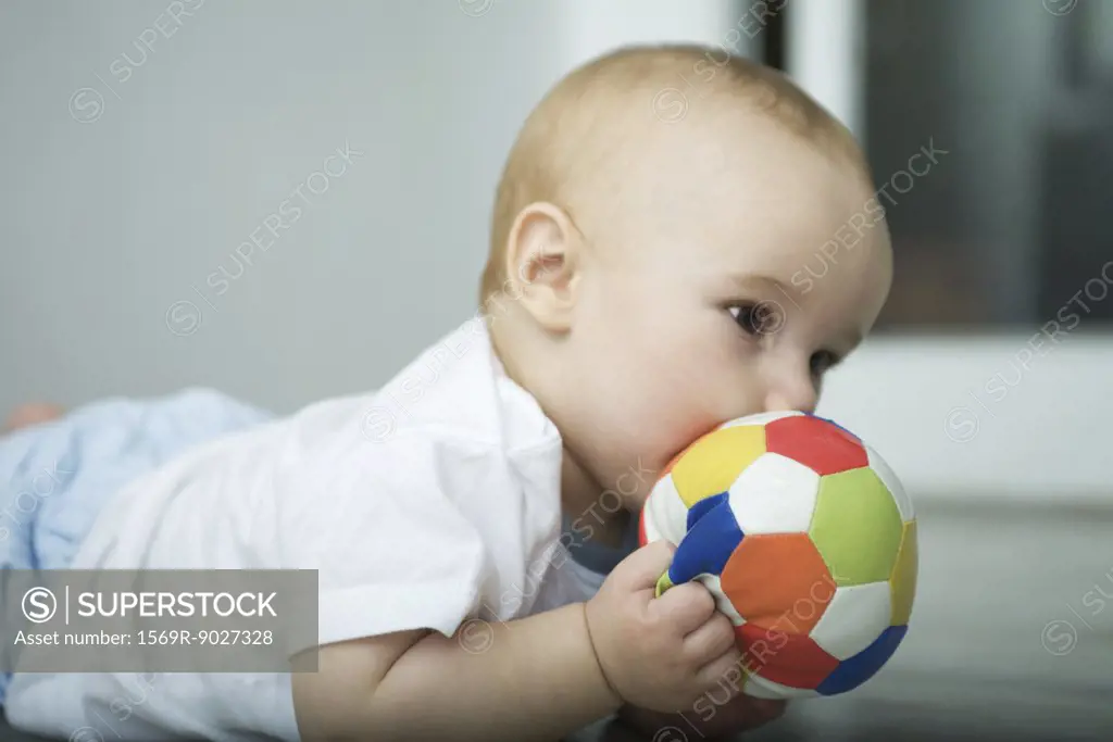 Baby on floor, holding ball up to mouth