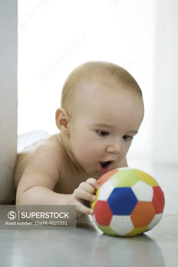 Baby lying on floor, holding ball, mouth wide open
