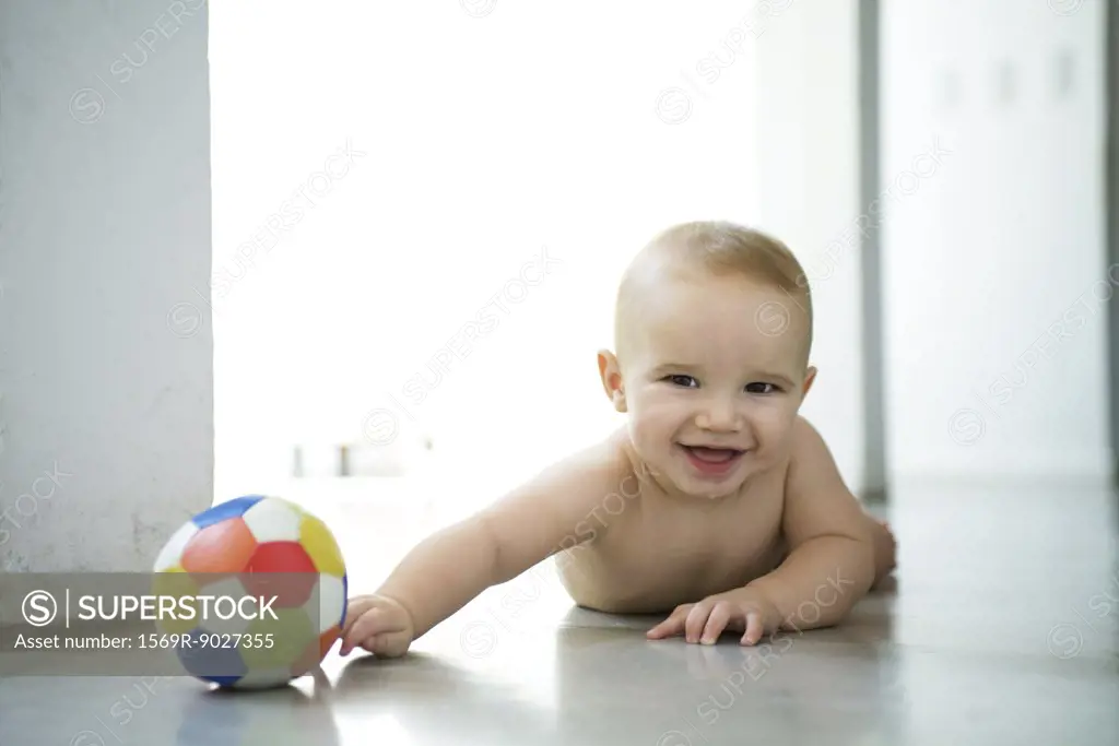 Baby lying on floor with ball, laughing and looking at camera