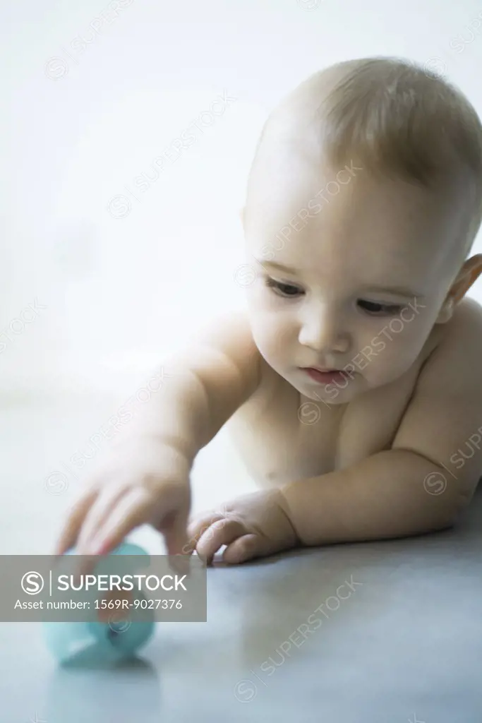 Baby lying on floor, reaching for rubber duck