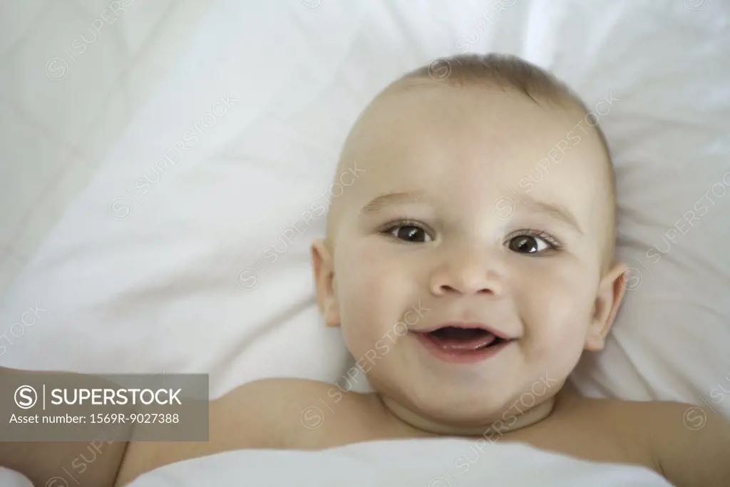 Baby in bed, under covers, smiling