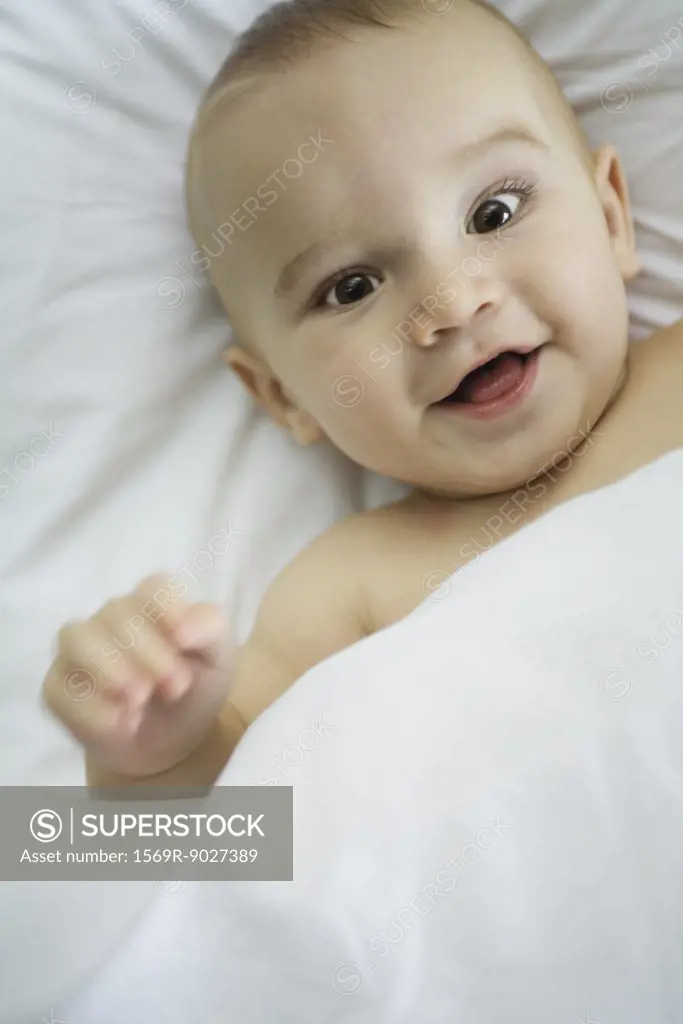 Baby in bed, under covers, smiling at camera