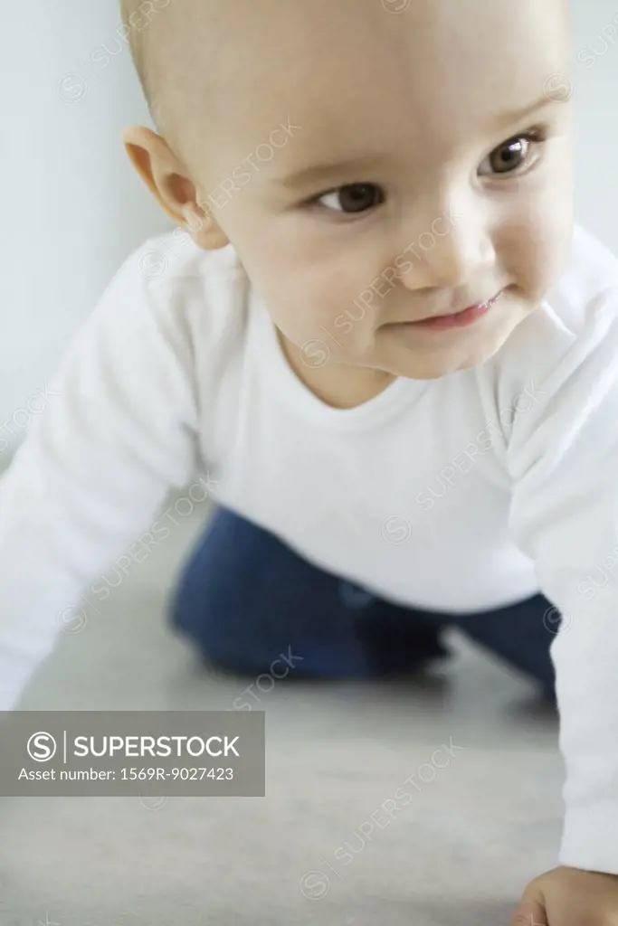 Baby crawling on floor, looking away, smiling, close-up