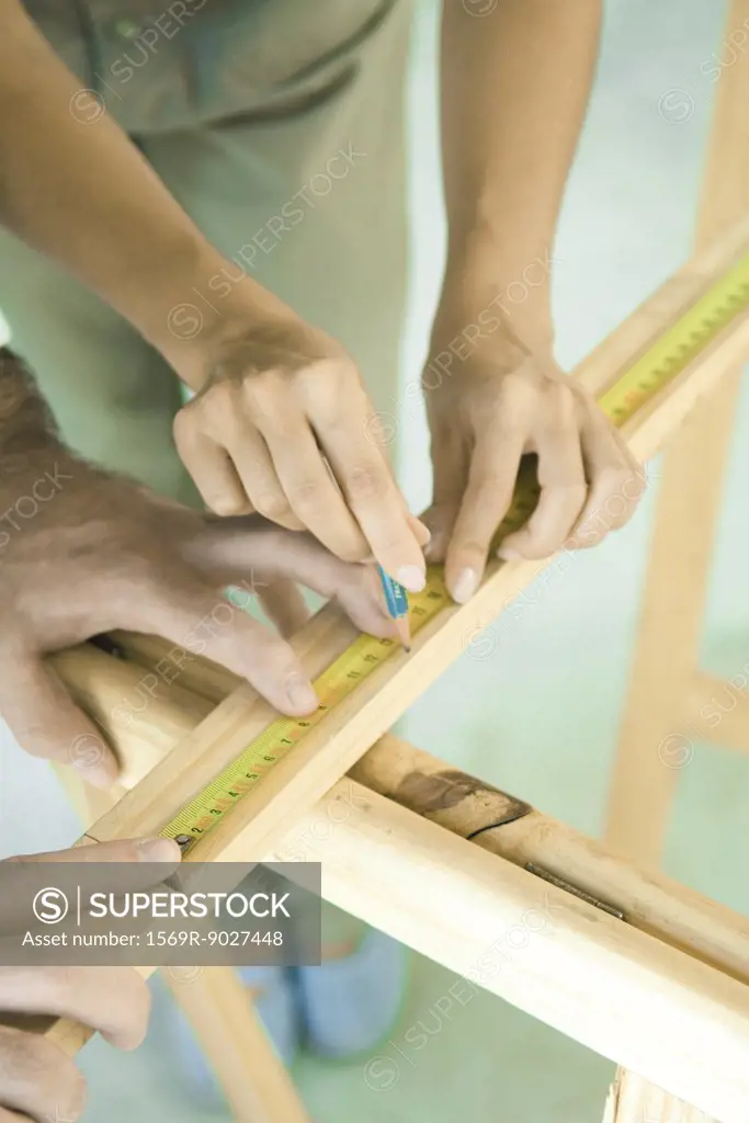 Couple measuring and marking piece of wood, close-up of hands