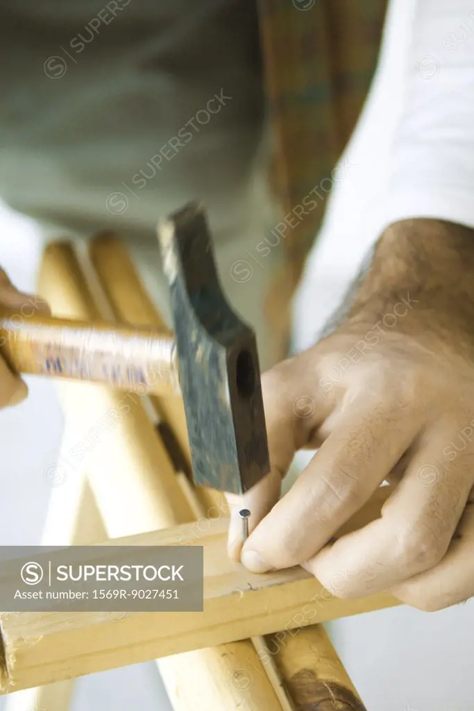 Man hammering nail into piece of wood, close-up of hands