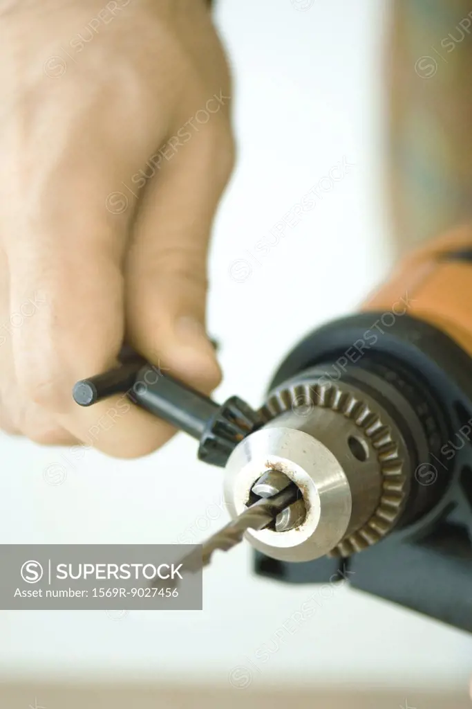 Man tightening drill bit, close-up of hand and drill