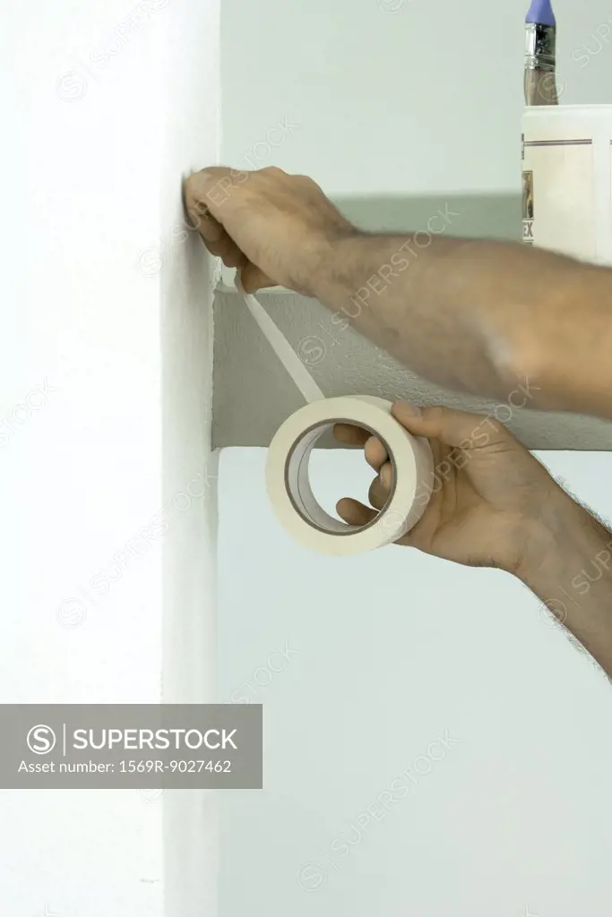 Man applying masking tape to wall, close-up of arms