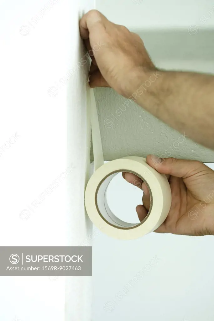 Man applying masking tape to wall, close-up of hands