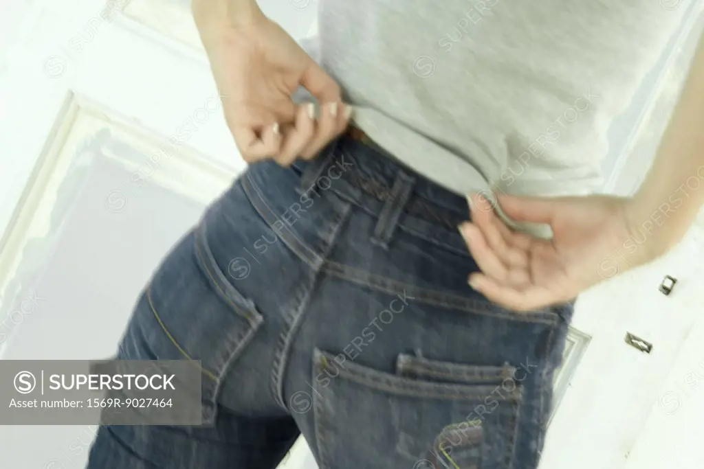 Woman untucking shirt from waist of jeans, close-up, rear view