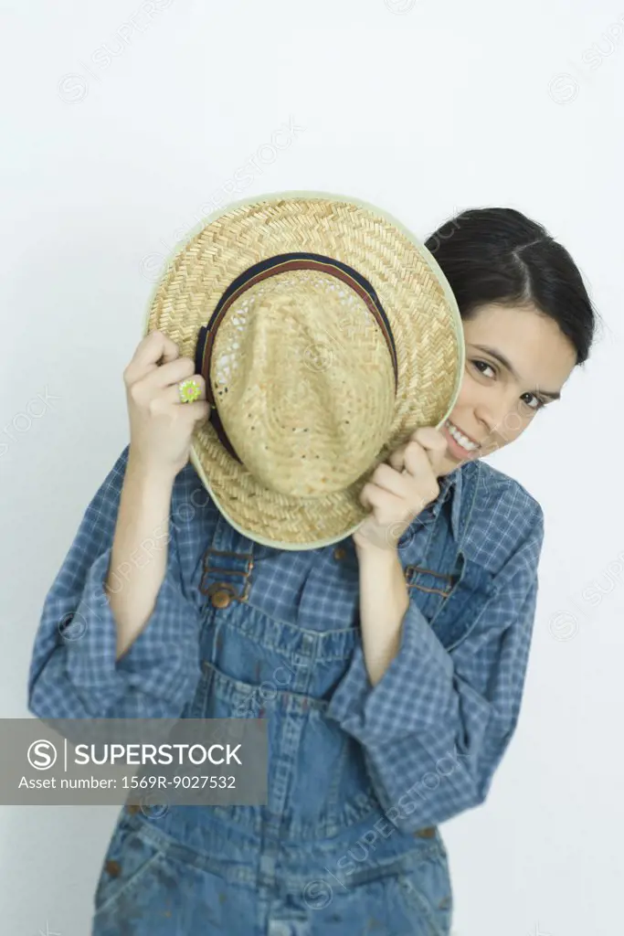 Teenage girl holding hat in front of face, smiling at camera