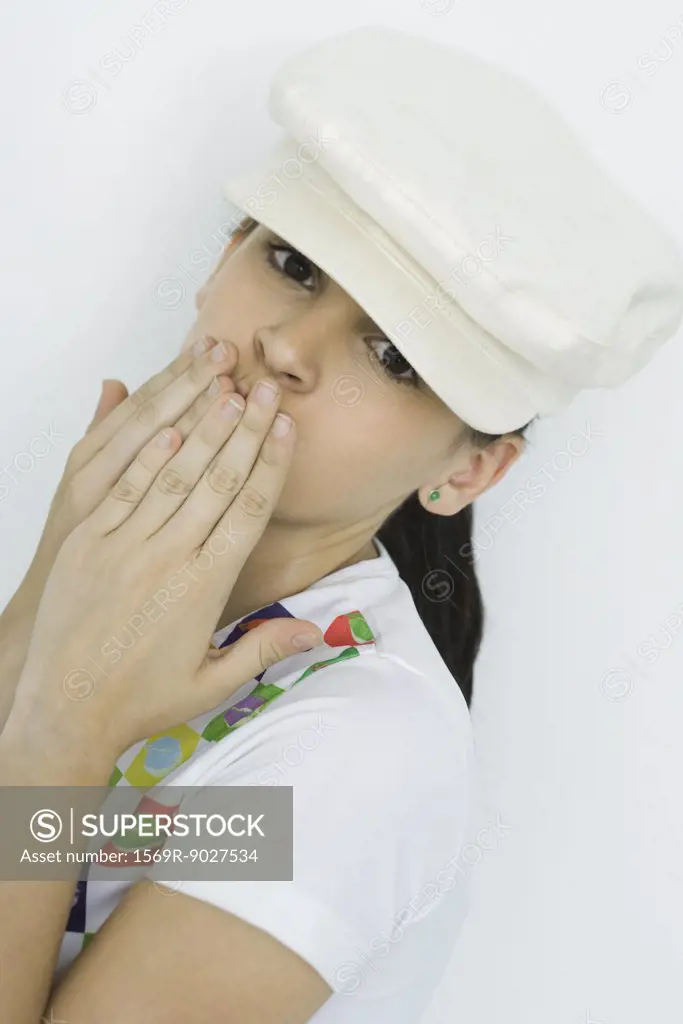 Teenage girl covering mouth with hands, looking at camera, portrait