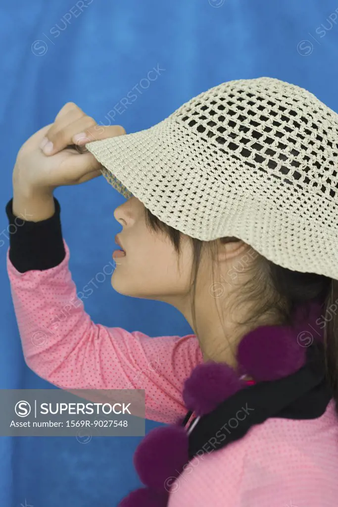 Teenage girl pulling sun hat over eyes, side view, portrait