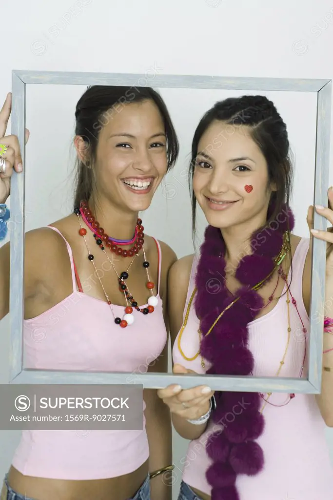 Two young friends holding up frame together, smiling at camera, portrait