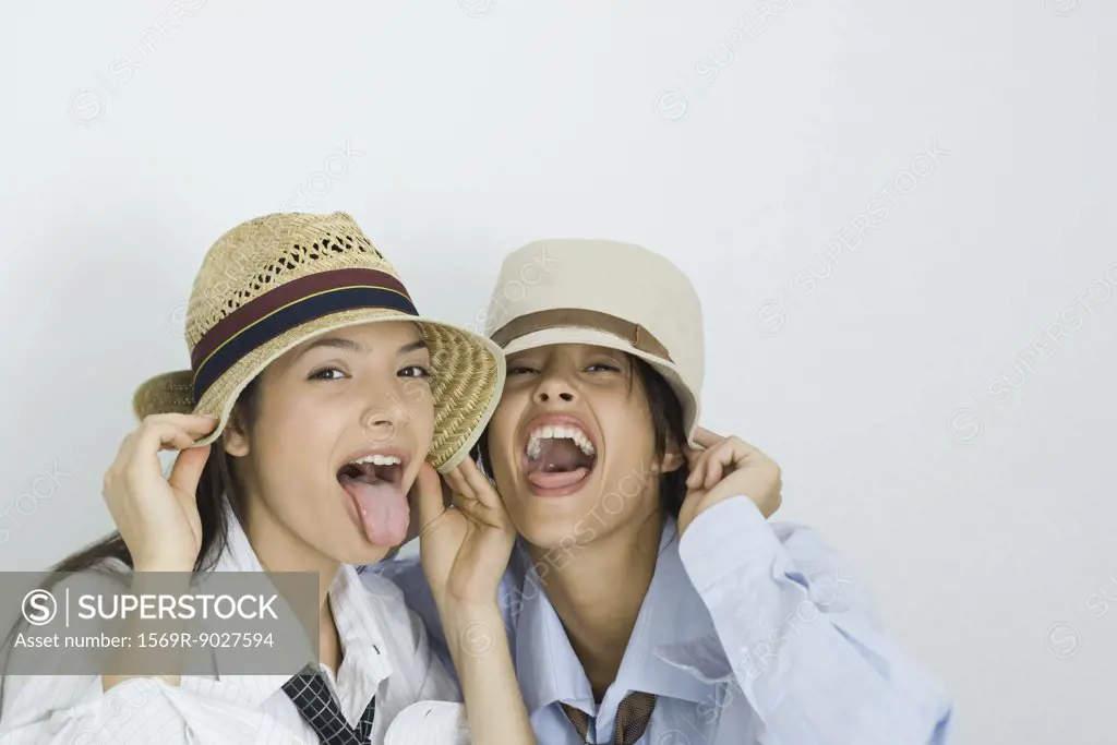 Two young friends wearing hats, sticking out tongues, looking at camera, portrait