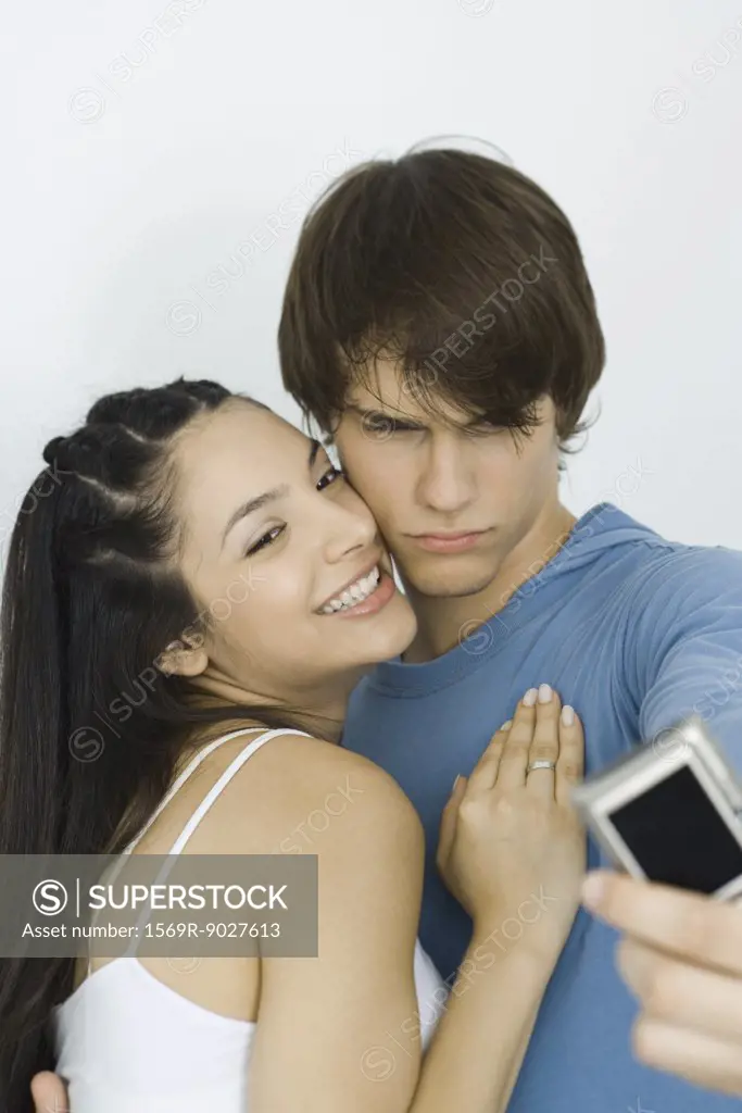 Young couple taking self portrait with digital camera, woman smiling, man furrowing brow