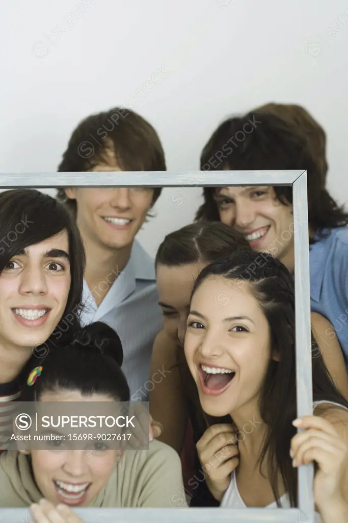 Young friends holding up frame together, smiling at camera