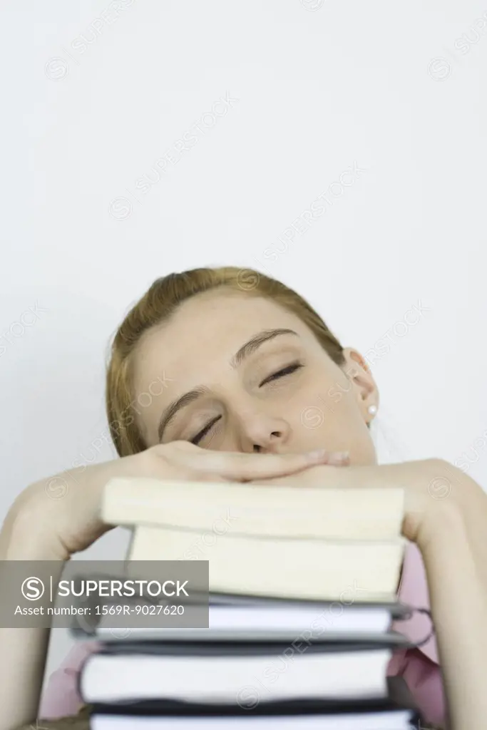 Young woman leaning on stack of books, eyes closed