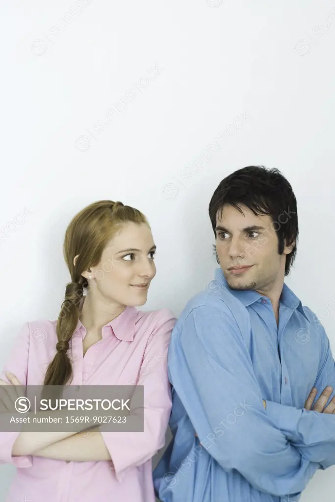 Young couple looking at each other over their shoulders, arms folded